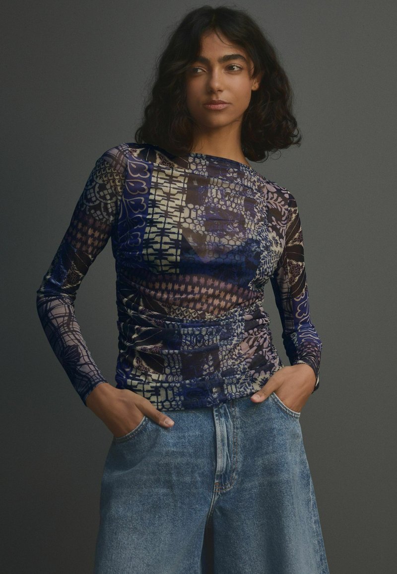 Top à manches longues en tissu léger et à motifs dans des nuances de bleu et de violet, avec des détails de fronces et un col rond.