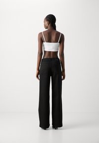 Black wide-leg jeans with a high waist and back pockets, paired with a fitted white cropped top featuring thin straps. Smooth fabric texture.