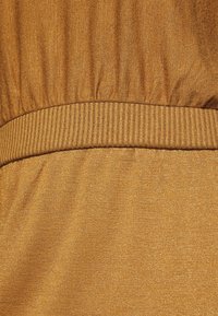 Tissu texturé dans une teinte doré-brun chaud avec une taille froncée et des accents côtelés. Surface lisse avec un léger brillant et un matériau extensible.