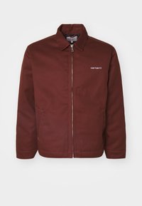 Burgundyröd jacka i kraftig tyg med dragkedja, spetsig krage, framfickor och subtil logotypdetalj på vänster bröst.