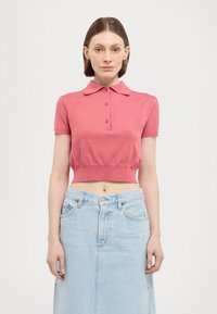 Rosa kort polo med korte ærmer, knaplukning og ribbet kant, parret med en lyseblå denimnederdel. Glat tekstur.