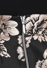 Černá látka s květinovým vzorem v metalických odstínech růžového zlata. Obsahuje kovový zip se značkou "YKK" a texturované detaily tkaniny.