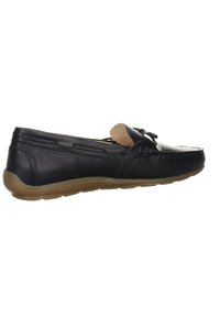 Zapato de mocasín de cuero negro con puntera redondeada, lazo decorativo y suela de goma flexible. Presenta costuras decorativas a lo largo de los lados.