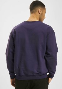 Sweatshirt din fleece violet cu decolteu rotund și manșete strâmte. Țesătura pare moale, cu o textură netedă și o croială lejeră.