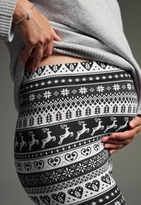 Sorte og hvide leggings med mønster af træer, hjerter, rensdyr og snefnug. Lavet af et blødt, strækbart materiale med en tætsiddende pasform.