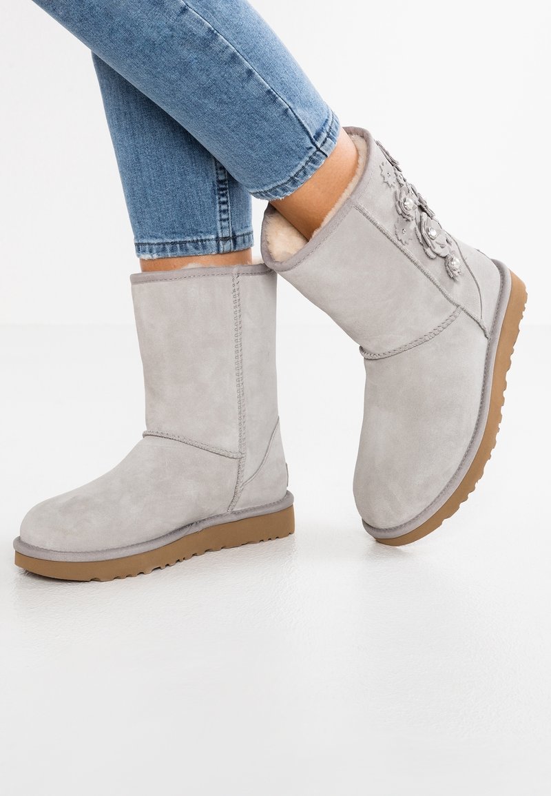 Bottes d'hiver en daim gris clair avec des accents floraux, portées avec un jean bleu, dotées de semelles en caoutchouc beige et d'une doublure intérieure douce.