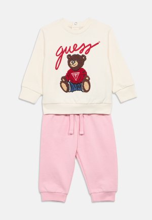 Zweiteiliges Kinderoutfit: elfenbeinfarbener Pullover mit gesticktem Bärenmotiv und dem Schriftzug "guess", kombiniert mit weichen rosa Jogginghosen.