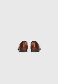 Zapatos de vestir de cuero marrón, tipo mocasín, mostrados desde atrás sobre un fondo liso de color gris claro.