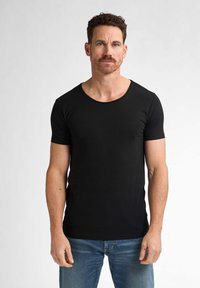 Tricou negru cu mânecă scurtă, într-un design ajustat, cu decolteu rotund și țesătură netedă, purtat cu blugi din denim albastru.
