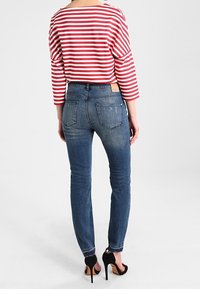 Červený a bílý pruhovaný top s dlouhým rukávem doplněný o úzké modré džíny. Tento outfit má jemnou texturu a detaily látky, které jsou podtrženy vysokými podpatky.