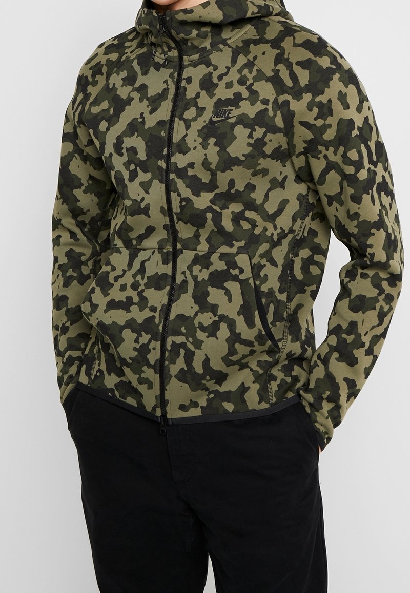 Maskovací zipová mikina v odstínech zelené a černé. Obsahuje kapuci, přední kapsy a malélogo na hrudi. Měkká, texturovaná tkanina.