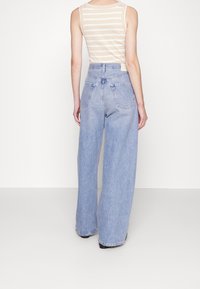 Jasnoniebieskie szerokie dżinsy z wysokim stanem, miękka tekstura denimu i tylne kieszenie. Połączone z beżowym topem w biało-beżowe paski.