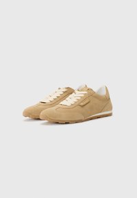 Le scarpe sportive in suede beige presentano una punta arrotondata, una superficie testurizzata, lacci larghi e una suola in gomma. I dettagli laterali includono cuciture decorative.