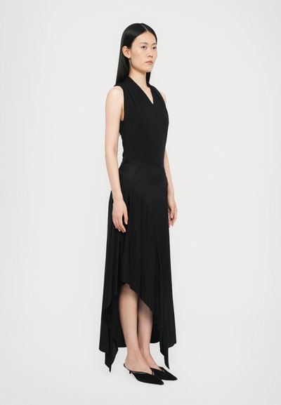 Black sleeveless dress with a v-neck, asymmetrical hem, flowing fabric, and smooth texture, paired with pointed black mules.