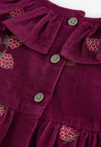 Syvän purppuranvärinen corduroy-kangas, vihreät napit, röyhelökaulus ja punaiset brodeeratut marjakimput vaatteiden yksityiskohdissa.