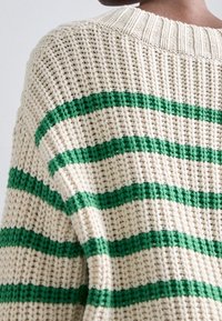 Pull en tricot crème avec des rayures horizontales vertes, présentant un motif texturé et un col côtelé.