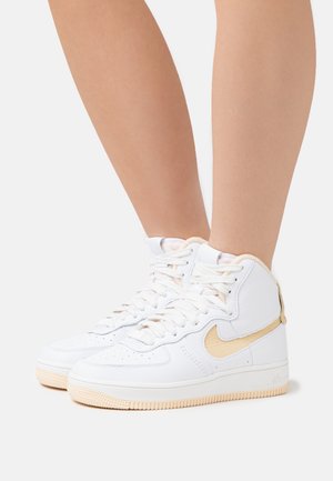 Legs wearing white high-top sneakers with beige soles and beige Nike swoosh, shown against a plain light background.
