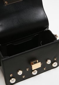Borsa a mano in pelle nera con una texture liscia, componenti in metallo dorato, dettagli in perla e chiusura a scatto rettangolare. L'interno è suddiviso in scomparti.