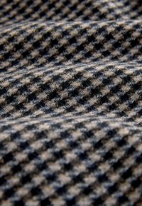 Tessuto con motivo pied de poule in nero e beige, caratterizzato da una superficie morbida e testurizzata disposta in pieghe ondulate.