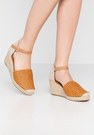 Koturny z pomarańczowym, plecionym przodem, beżową tkaniną z tyłu i regulowanym, brązowym paskiem wokół kostki; podeszwa owinięta jutą; teksturowana powierzchnia.