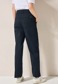 Marineblauwe katoenen broek met een elastische tailleband, rechte pijpen, zijzakken en details op de achterzak, gedragen met witte sneakers.