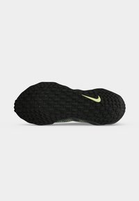 Σόλα μαύρου αθλητικού παπουτσιού Nike με μοτίβο που μοιάζει με πλέγμα και μικρό κίτρινο λογότυπο Nike κοντά στην μπροστινή πλευρά.