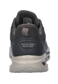 Skechers Slip-Ins negras con un upper de tela texturizada, collar acolchado y una suela acolchada con un detalle de logo prominente.