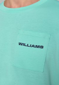 Miętowy t-shirt wykonany z miękkiego materiału, z kwadratową kieszonką z ciemnoniebieskim napisem "WILLIAMS", okrągłym dekoltem i krótkimi rękawami.
