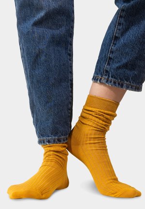 Żółte skarpetki w prążki o luźnym kroju, zestawione z podwiniętymi ciemnymi dżinsami, podkreślające żywy kolor i fakturę materiału.