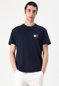 Marinefarbene Baumwoll-T-Shirt mit Rundhalsausschnitt und kurzen Ärmeln. Enthält ein kleines Logo auf der Brust in einem Rechteck in Rot und Weiß.