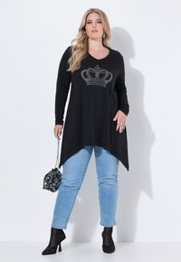 Czarna bluzka z długim rękawem z srebrnym wzorem korony, zestawiona z jasnoniebieskimi dżinsami z perełkowymi ozdobami. Całość uzupełniają czarne szpilki i cekinowa torebka.