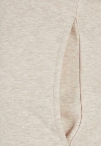Beige sweatshirt close-up, met een zachte textuur en een zijzak met een naaddetail. De stof heeft een subtiel gemêleerd patroon.