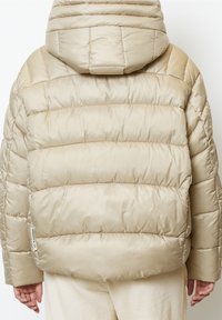 Béžová prošívaná bunda s kapucí, s prošívanou texturou a mírně oversized střihem. Obsahuje štítek na bočním švu.