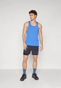 Blue athletic tank top with a rounded neckline, paired with black shorts featuring a white logo. Black sports shoes and blue socks complete the look.