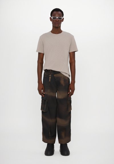 Beige t-shirt med kort ärm, svarta cargobyxor med bruna och beige fläckar, och svarta kraftiga kängor. Tillbehör inkluderar vita solglasögon.