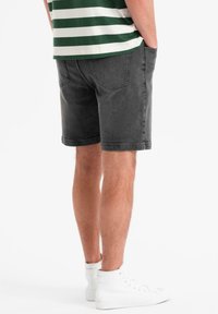Shorts en denim gris pour homme avec poches, coupe droite et ourlets retroussés, associés à une chemise rayée verte et blanche et des baskets montantes blanches.