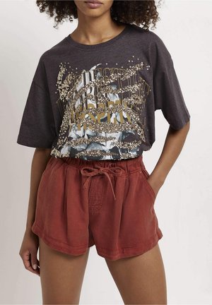 T-shirt graphique gris avec motifs dorés et bleus, associé à un short à cordon de couleur rouille avec poches latérales et coupe décontractée.