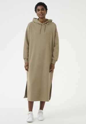 Hoodie, lange mouw sweatshirt jurk in lichtbruine stof met zijsplitten en geborduurde details, gecombineerd met witte sneakers.