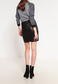 Gonna mini in pelle nera, design aderente. Abbinata a una maglietta a maniche lunghe a righe bianche e nere. Modella che indossa stivaletti neri alla caviglia con zip.