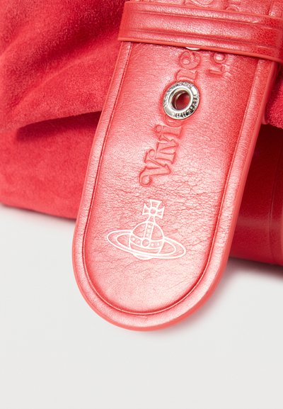 Κοντινή λήψη υφασμένης κόκκινης δερμάτινης λωρίδας με ανάγλυφο λογότυπο και λεπτομέρεια ασημένιου μεταλλικού κρίκου σε ταιριαστό κόκκινο υφασμάτινο φόντο.