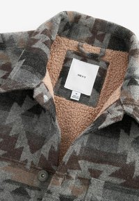 Grå och brun mönstrad flanellskjorta med mjuk beige fleecefoder, knappstängning och etikett inuti kragen. Texturerad tygdesign.