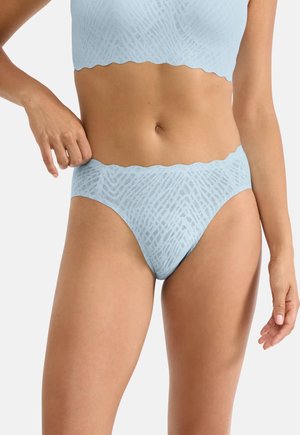 Woman wearing light blue textured high-cut underwear and matching crop top, holding waistband with one hand against a white background.