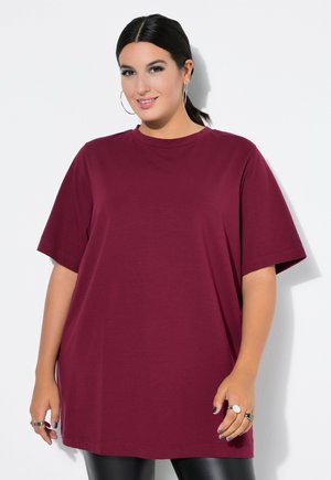 T-shirt oversize in cotone bordeaux con maniche corte, colletto rotondo e vestibilità rilassata, abbinato a leggings neri e dettagli di gioielli argentati.