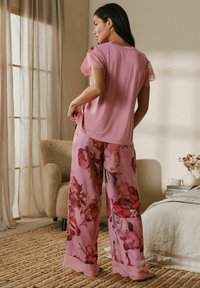 Ružový top s čipkovanými rukávmi v kombinácii s ružovými nohavicami s kvetinovým vzorom a čipkovanou lemovkou. Hladká textúra a voľný strih.