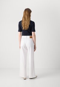 White wide-leg trousers with a back patch pocket, paired with a fitted navy top. Smooth fabric with subtle stitching details.