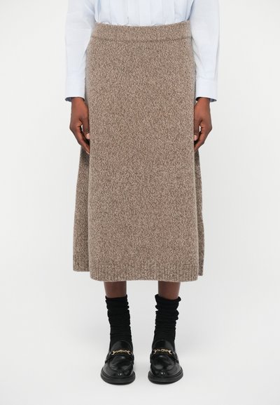Jupe en tricot en tissu texturé brun, de longueur mi-mollet avec une taille ajustée. Assortie à des chaussettes noires superposées et des mocassins.