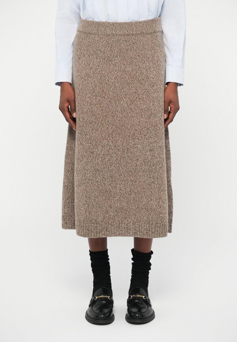 Πλεκτή φούστα από υφή καφέ ύφασμα, μήκους μέσης γάμπας με εφαρμοστό λάστιχο. Συνδυασμένη με μαύρες στρωματωτές κάλτσες και loafers.