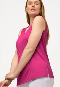Fuchsia ärmelloses Oberteil mit rundem Ausschnitt, seitlichen Schlitzen, glatter Textur und lockerer Passform, kombiniert mit weißen Hosen.