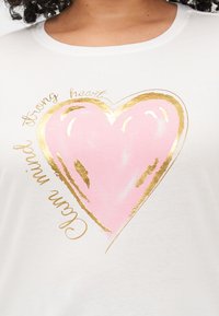 Tricou alb din bumbac, cu un grafic mare în formă de inimă roz conturat în aur, având textul "minte calmă" și "inimă puternică" scris în cursiv auriu.