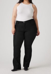 Jeans de mezclilla negra acampanados con cintura alta y bolsillos frontales, combinados con una camiseta de tirantes blanca de canalé. El material parece suave con un ligero elástico.